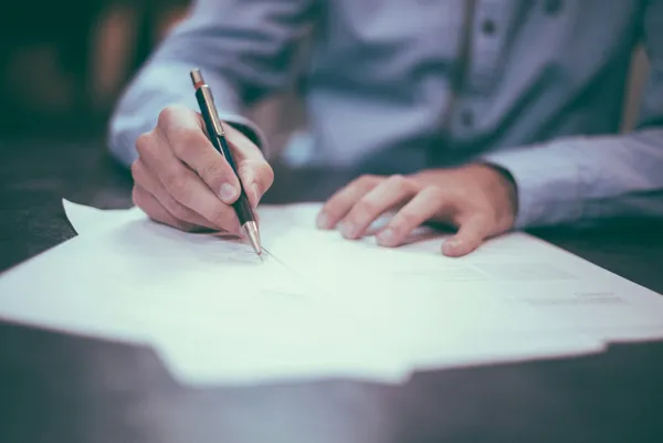 Person signerer et lånedokument med selvskyldnerkausjon ved et skrivebord